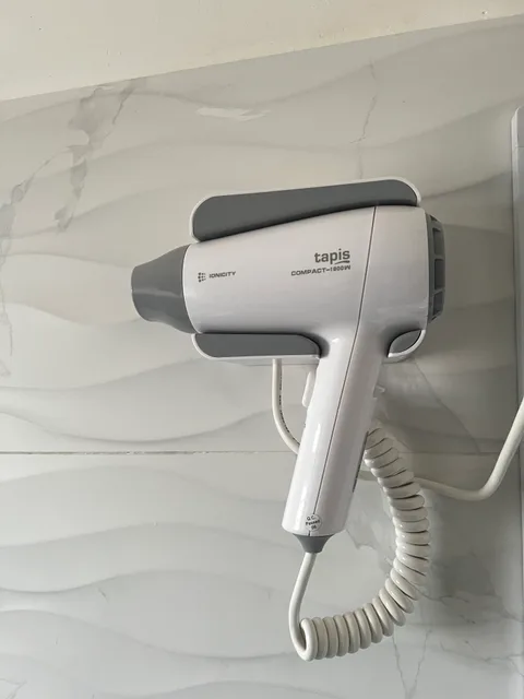 A wall-mounted hair dryer with its coiled cord against cream bathroom tiles at Wangs BnB.