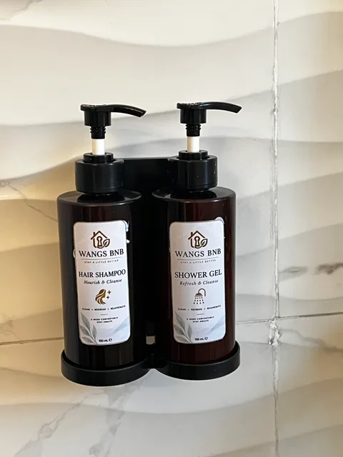 Wangs BnB shampoo and shower gel in wall-mounted pump bottles against cream bathroom tiles.
