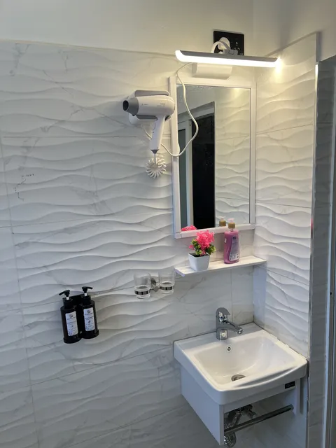 Astra bathroom basin and mirror with a hair dryer, mirror light and toiletries against textured white tiles.
