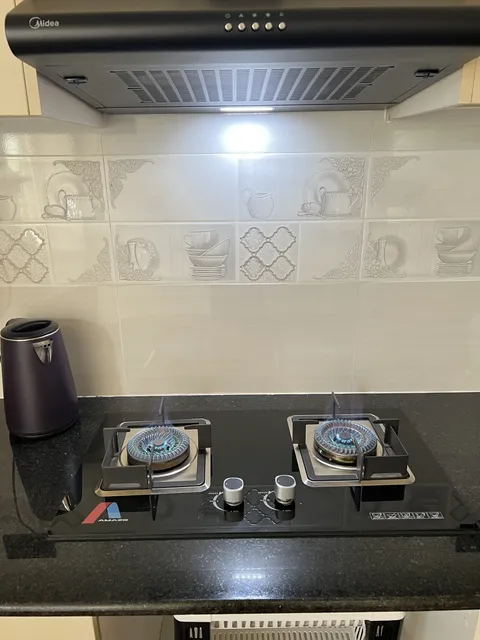 Astra two-burner hob and kettle beneath an extractor against textured white kitchen tiles.