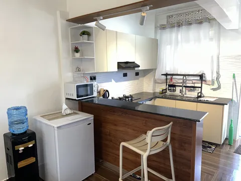 Astra kitchen and breakfast counter with a cream stool, refrigerator, microwave and cream cabinets.