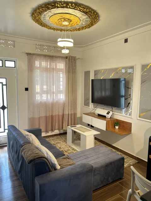 Astra living room with a grey corner sofa, white coffee tables and television on a gold-accented wall.