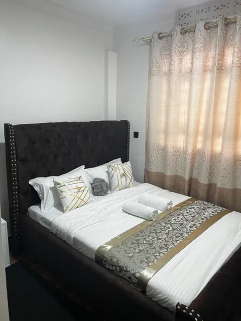 Astra main bedroom with a black buttoned headboard, white bedding, patterned cushions and rolled towels.