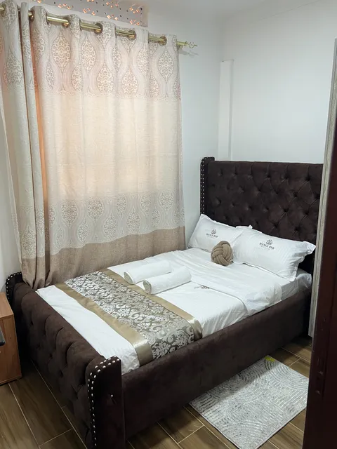 Astra second bedroom with a dark upholstered bed, white bedding and a patterned runner beside the window.