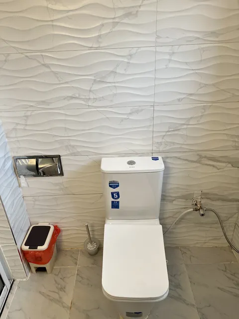 Astra toilet and handheld bidet spray beside the textured white bathroom wall.