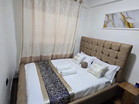 Luna main bedroom with a taupe upholstered headboard, white bedding, patterned runner, cushions and rolled towels beside the window.