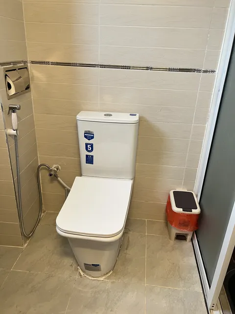 Luna bathroom with a toilet and handheld bidet spray against cream tiles.