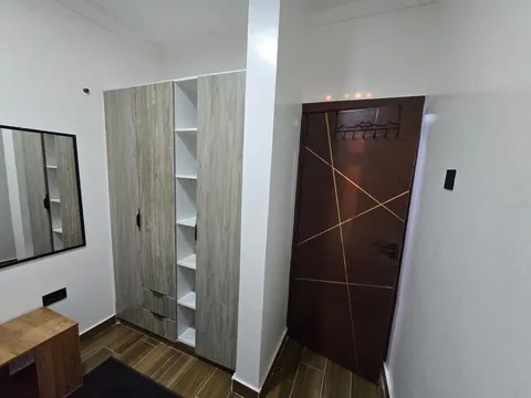 Nova bedroom wardrobe with shelves and drawers beside a wall mirror, wooden bedside unit and brown door with gold accents.