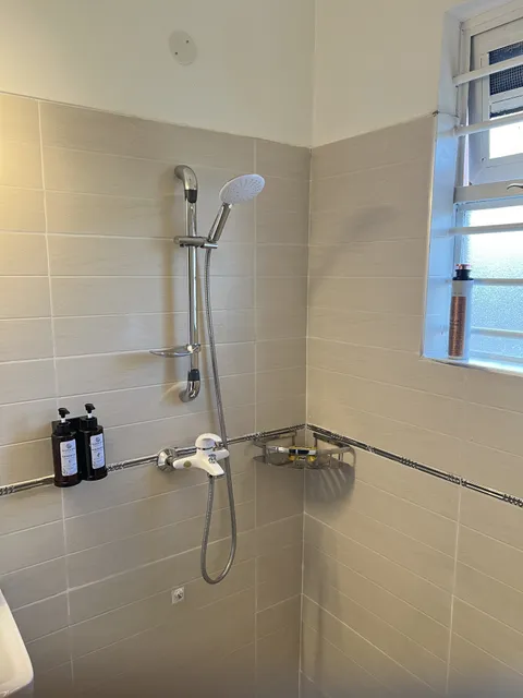 Bathroom shower fittings and wall-mounted toiletries beside the window against cream tiles.