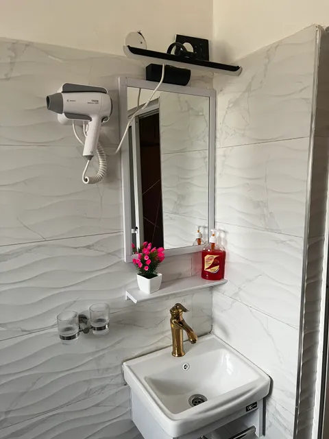 Sol bathroom basin with a gold-coloured tap, wall mirror, hair dryer and toiletries against white patterned tiles.