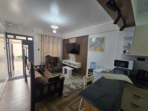 Sol living room and open kitchen, with a brown sofa, armchair, wall-mounted television and breakfast counter.