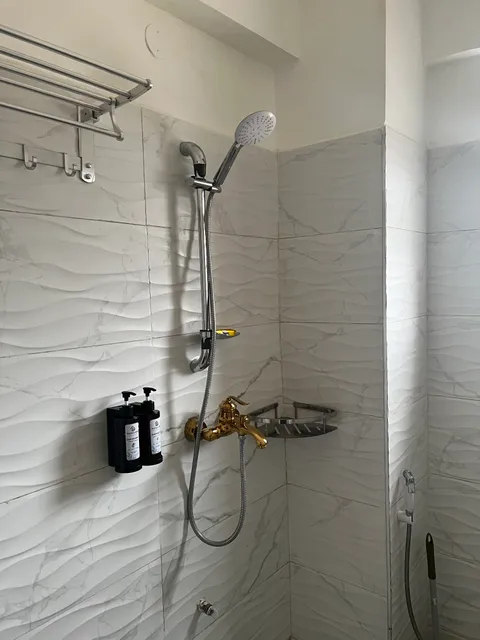 Sol shower area with a handheld shower, gold-coloured mixer tap, wall-mounted toiletries and towel rack against white tiles.