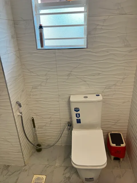 Sol bathroom toilet and handheld bidet spray beneath the window, surrounded by white patterned wall and floor tiles.